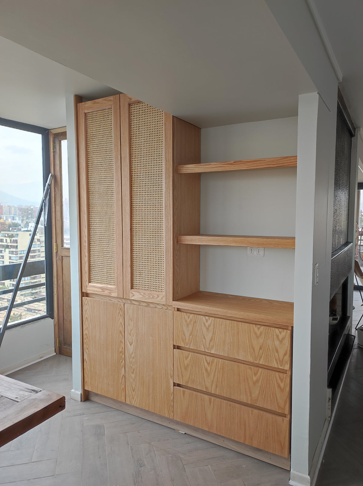 Mueble a medida en enchapado de encina con frentes de rejilla, repisas y cajones, hecho para el rincón de un ventanal