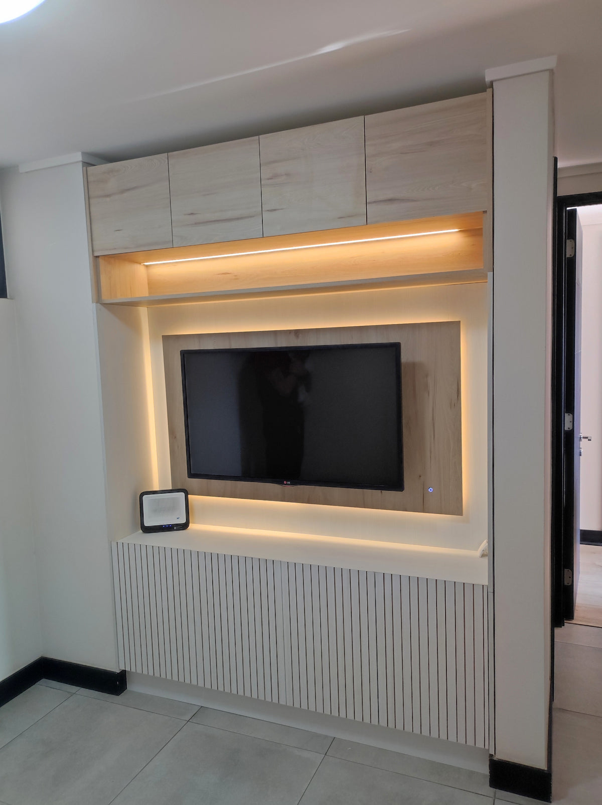 Mural de TV a medida con iluminación LED integrada, frente listoneado blanco y muebles altos de guardado